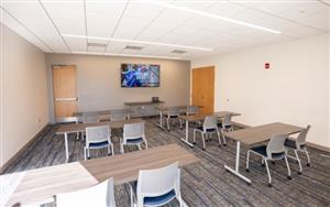 A meeting room with tables, chairs, and carpeted flooring.